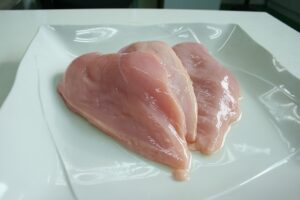 Immagine di un pollo crudo su un tagliere, circondato da ingredienti freschi per la cottura.