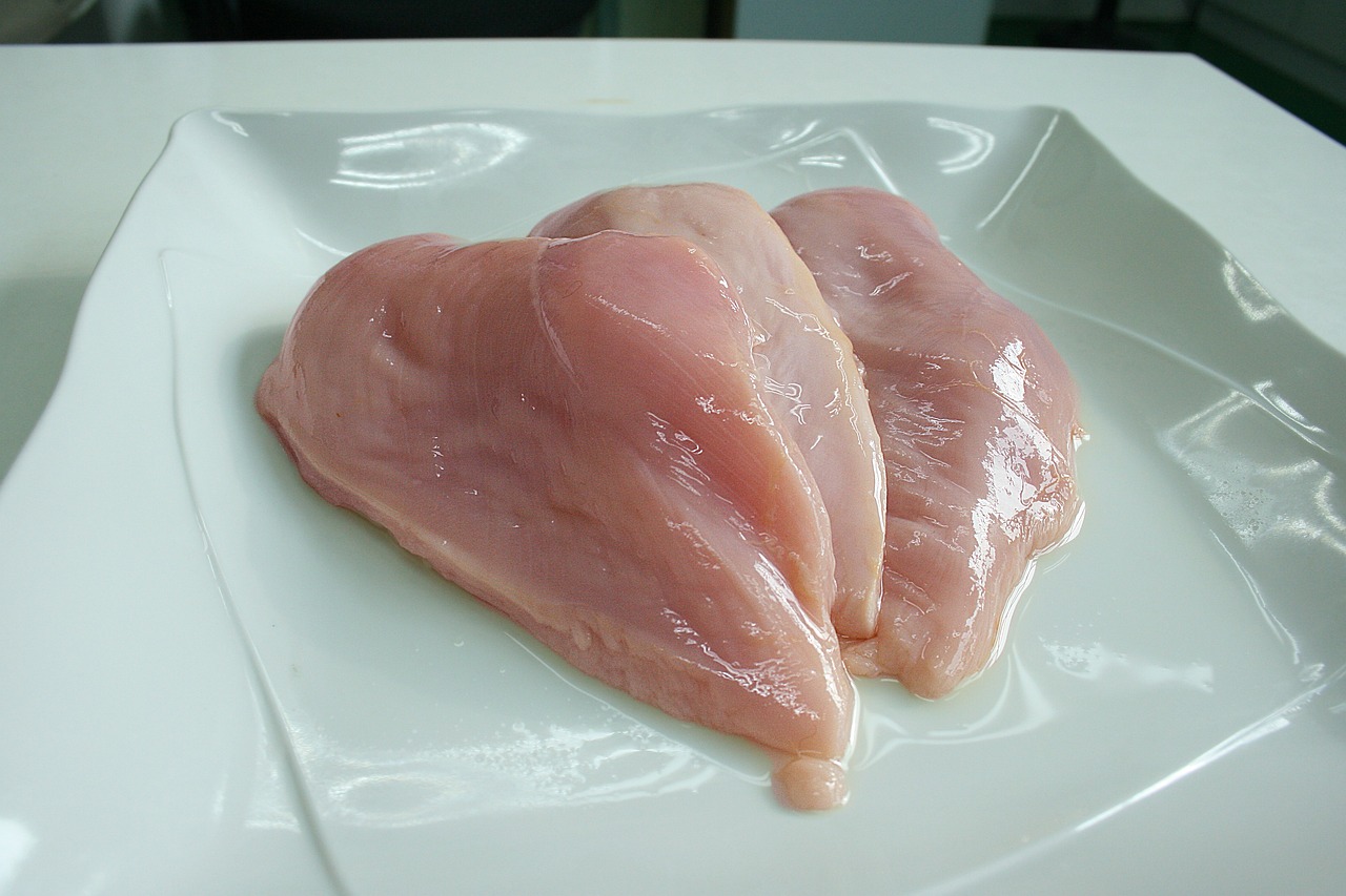 Immagine di un pollo crudo su un tagliere, circondato da ingredienti freschi per la cottura.