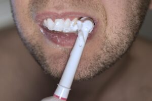 Uomo che tiene una tazza di caffè e spazzolino da denti, riflettendo su quando lavare i denti.